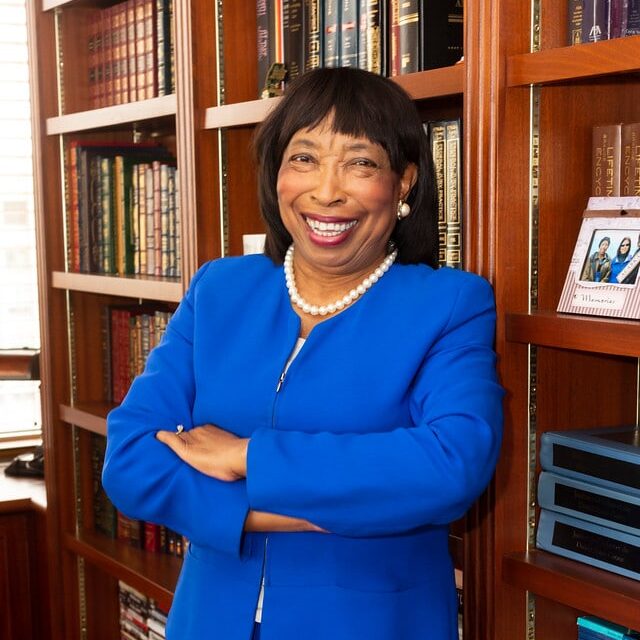 May contain a person smiling in front of bookshelves.