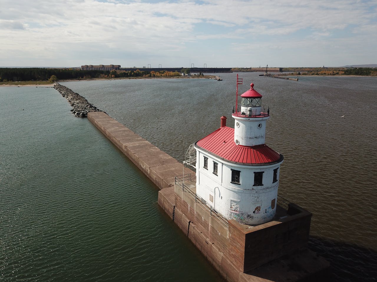May contain a lighthouse with a red roof on a concrete pier.