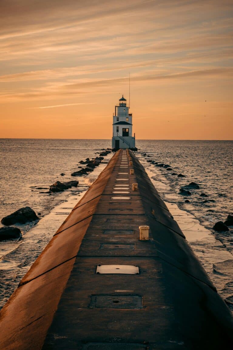 May contain a lighthouse at the end of a pier on the ocean at sunset.