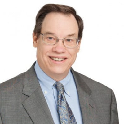 May contain a person wearing glasses, a blue shirt, and a grey suit.