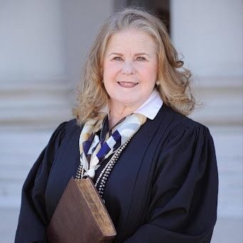 May contain one person in judicial robes holding a book.