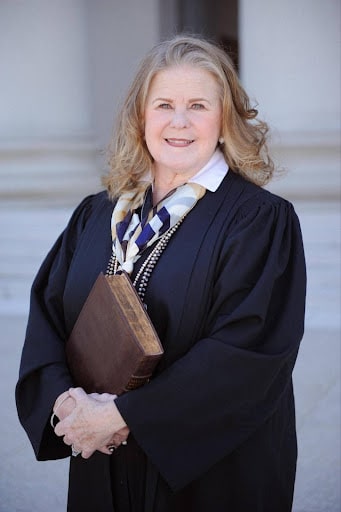 May contain one person in judicial robes holding a book.