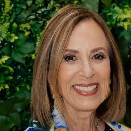 May contain one person smiling against a green foliage background.