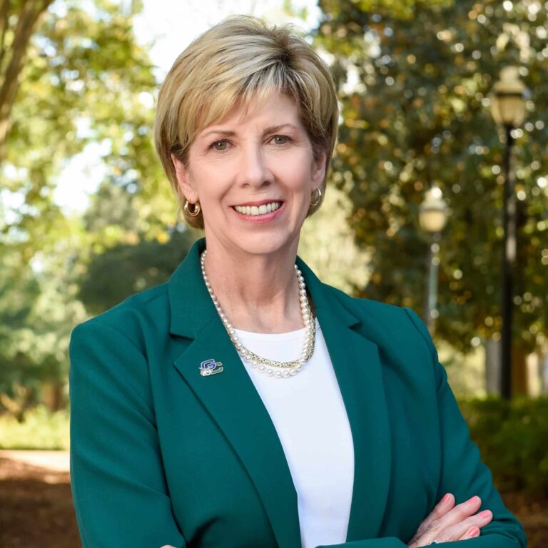 May contain one person wearing a green blazer and pearl necklace outdoors.