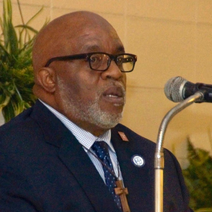 May contain one person wearing glasses and a suit speaking at a microphone.