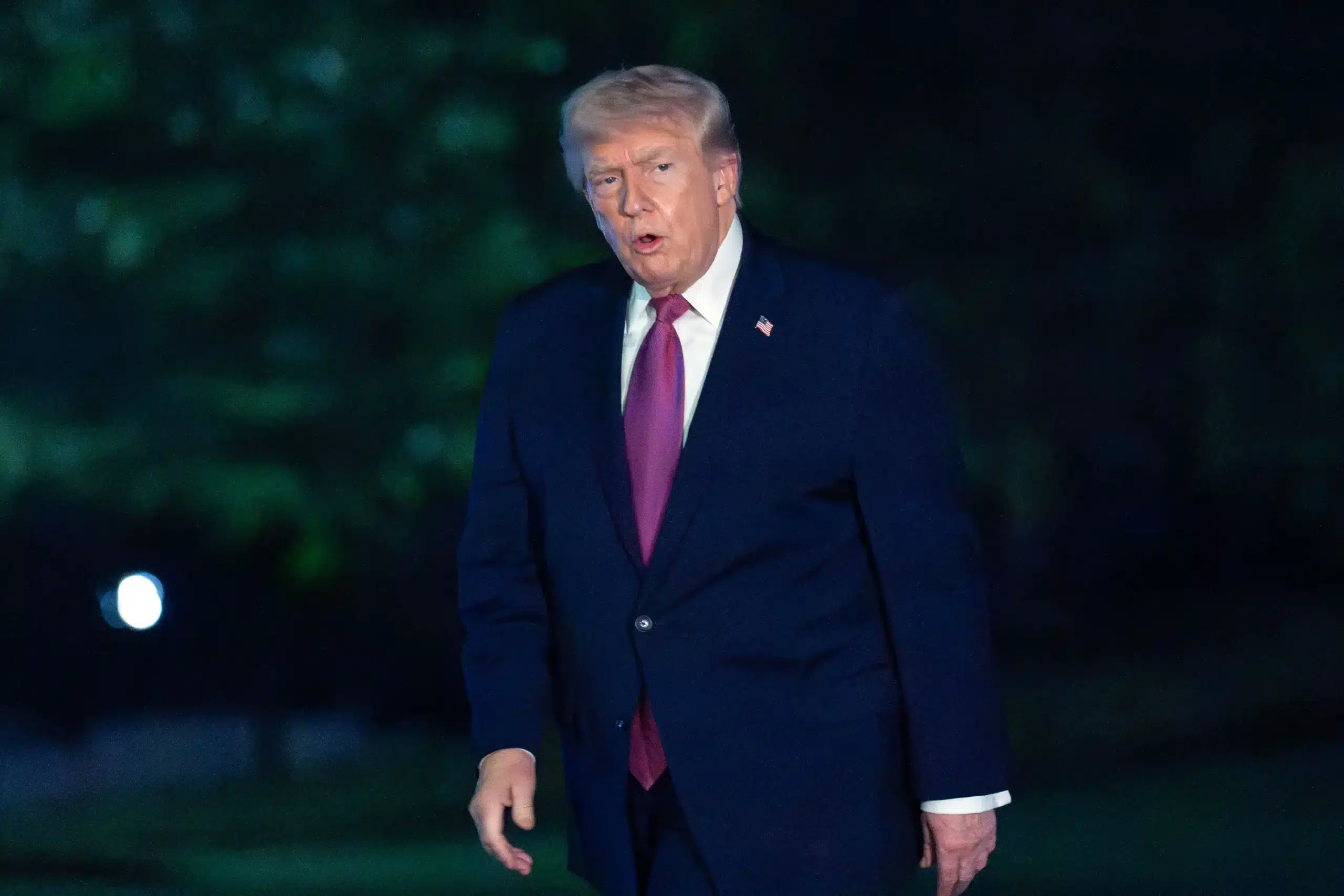 May contain one person wearing a dark suit and pink tie outdoors at night.