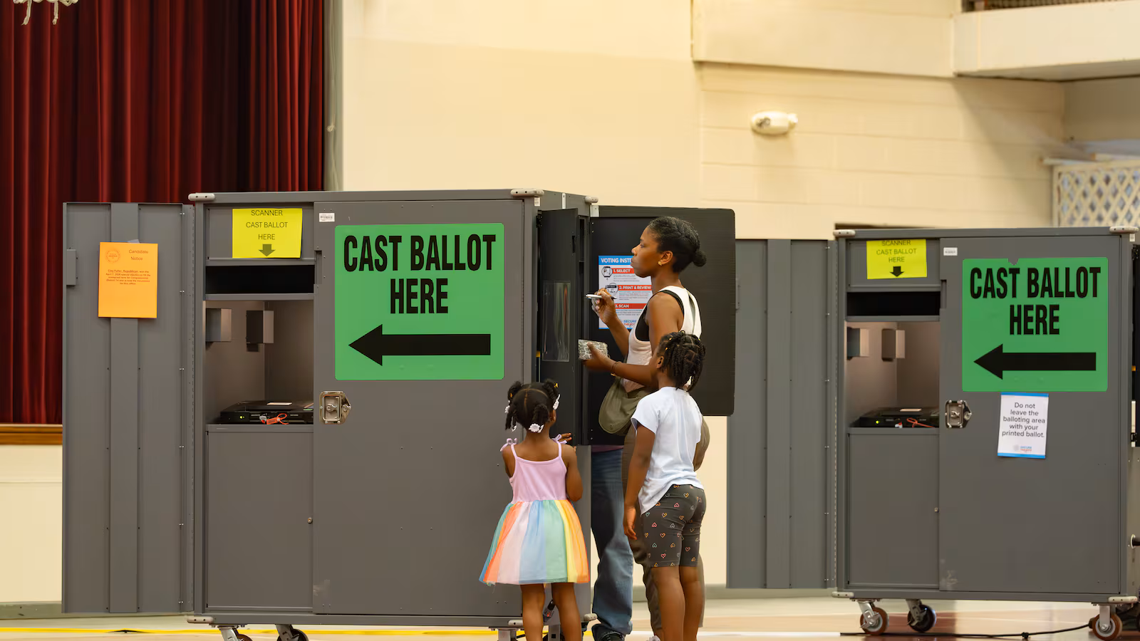 May contain three people near voting booths.