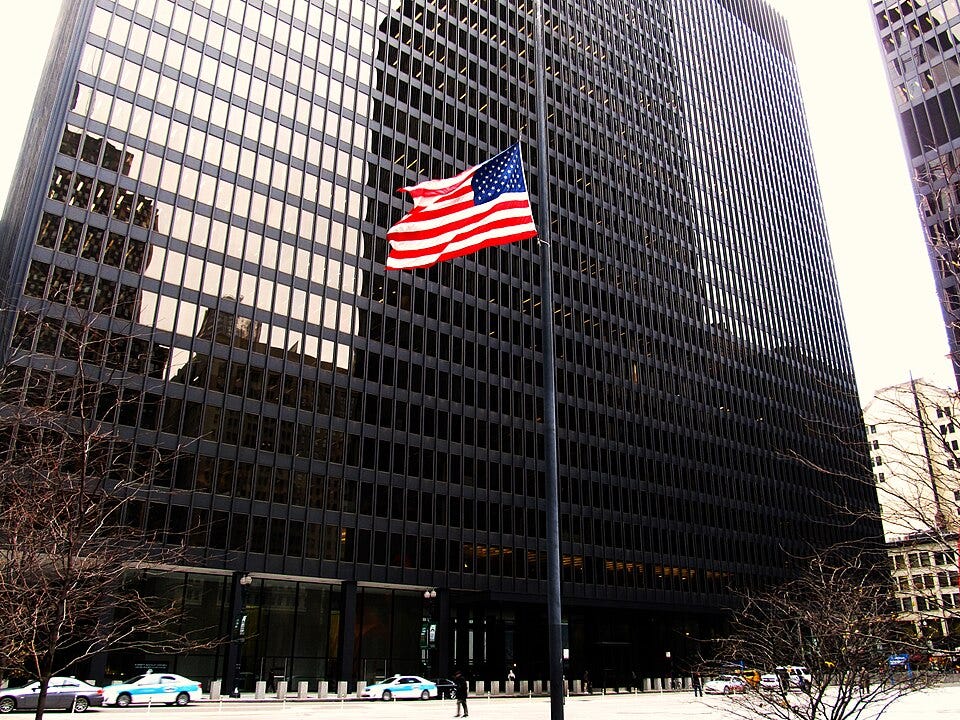 May contain an American flag in front of a modern building with cars.