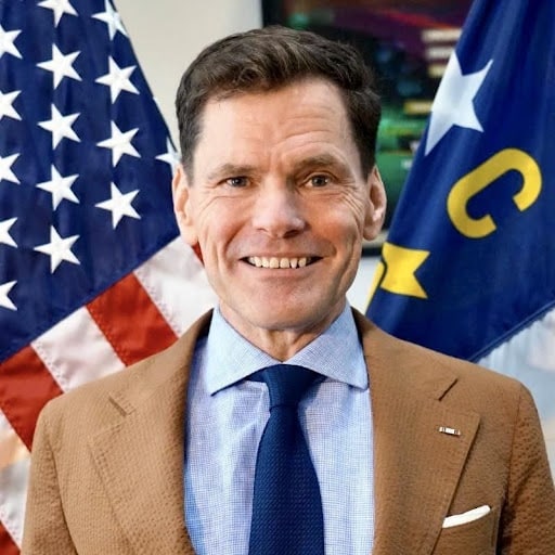 May contain a person smiling in front of two flags.