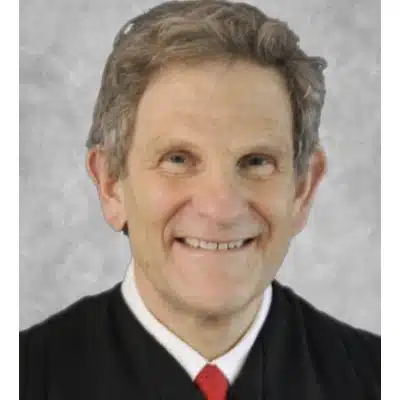 May contain one person smiling, wearing a black robe and red tie.