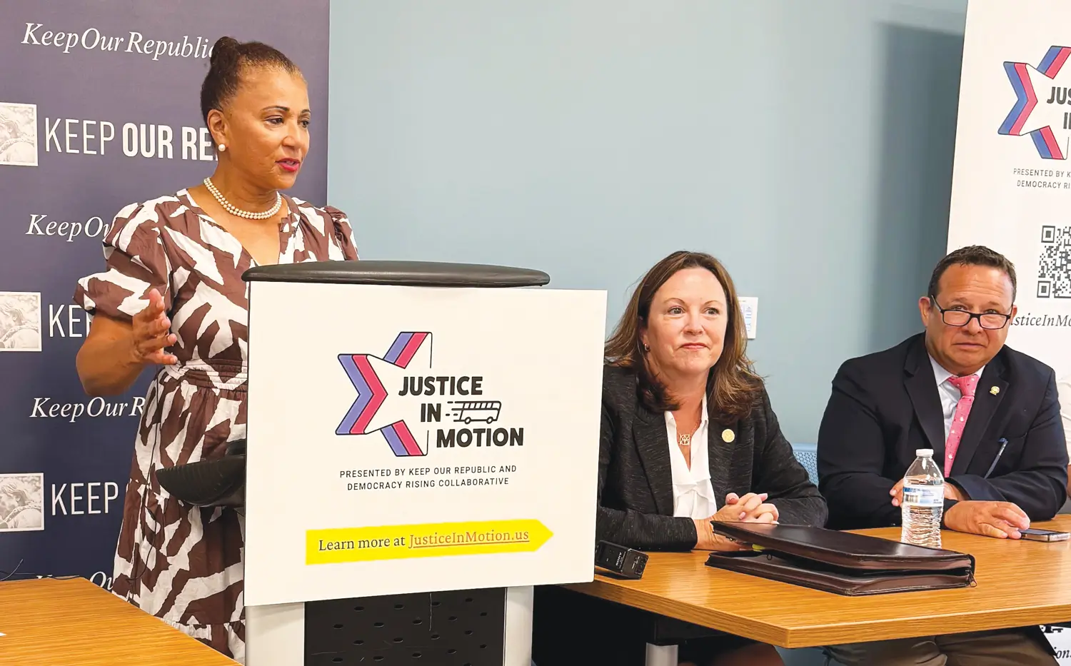May contain three people at a table with a speaker at a podium.