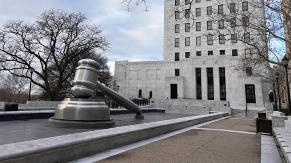 May contain a large metal gavel sculpture in front of a building.