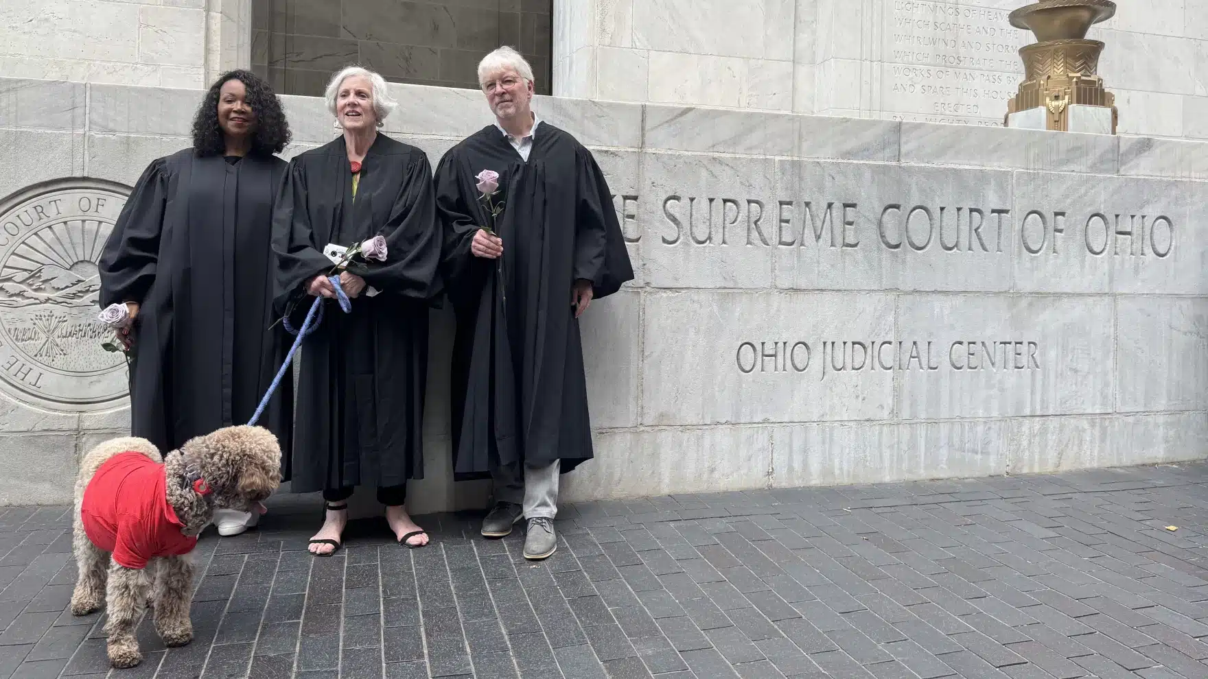 May contain three people in robes and a dog in a red shirt.
