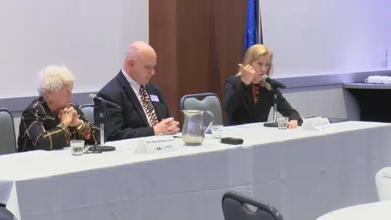 May contain three people at a table with microphones and name tags.