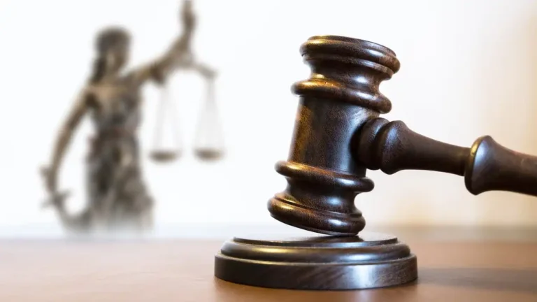 May contain a gavel and a blurred statue of justice with scales.