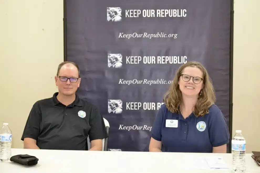 May contain two people sitting at a table in front of a banner that reads "KEEP OUR REPUBLIC".