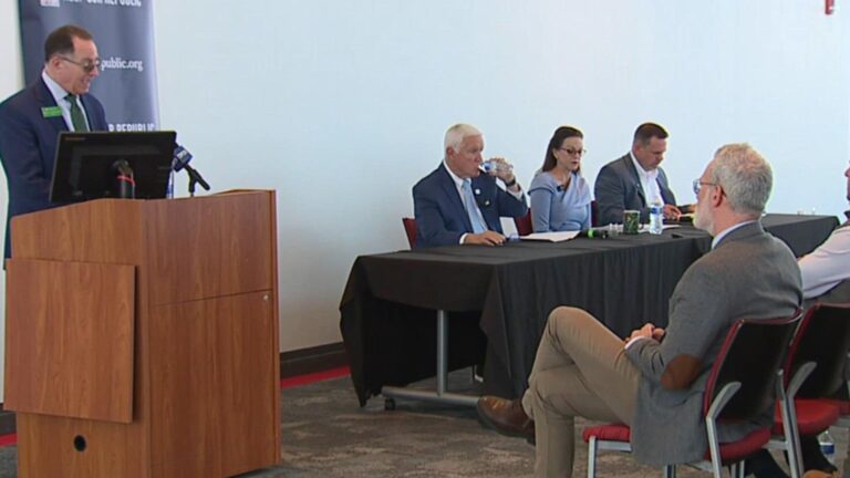 May contain five people at a table and one person at a podium.