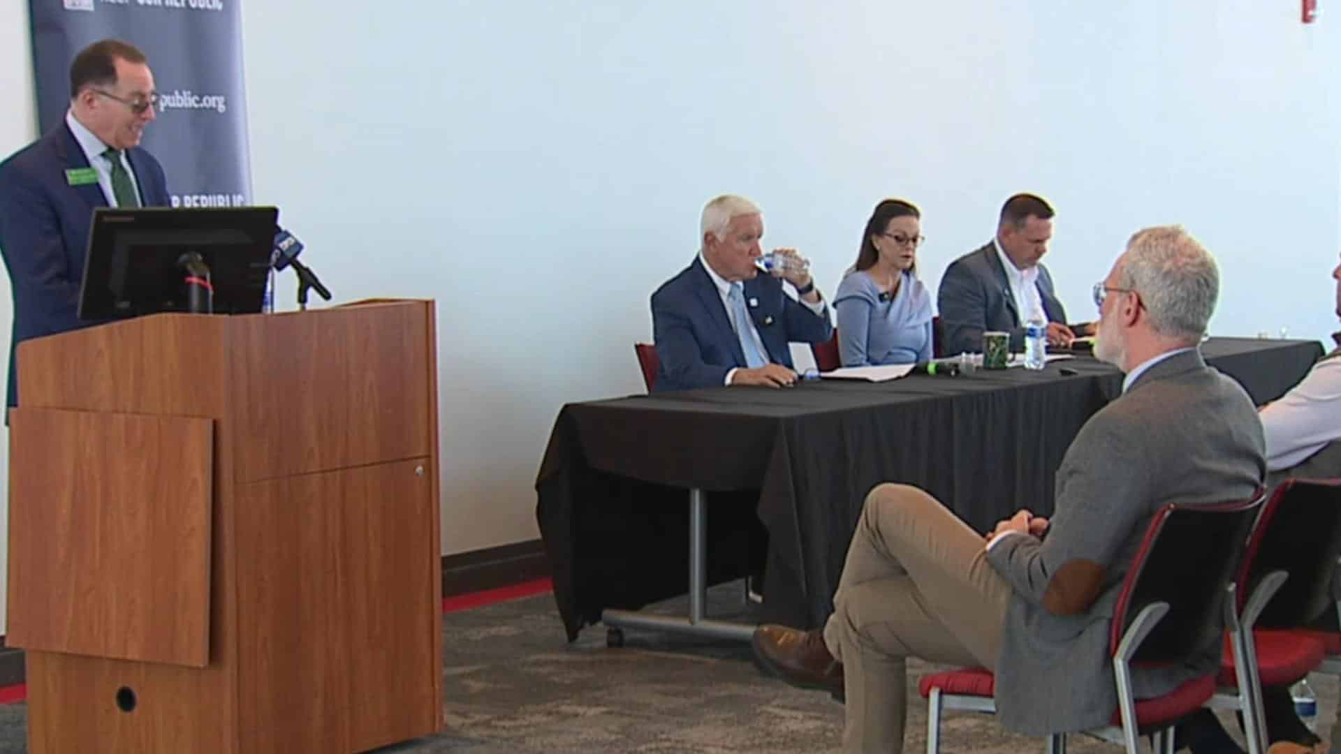 May contain five people at a table and one person at a podium.