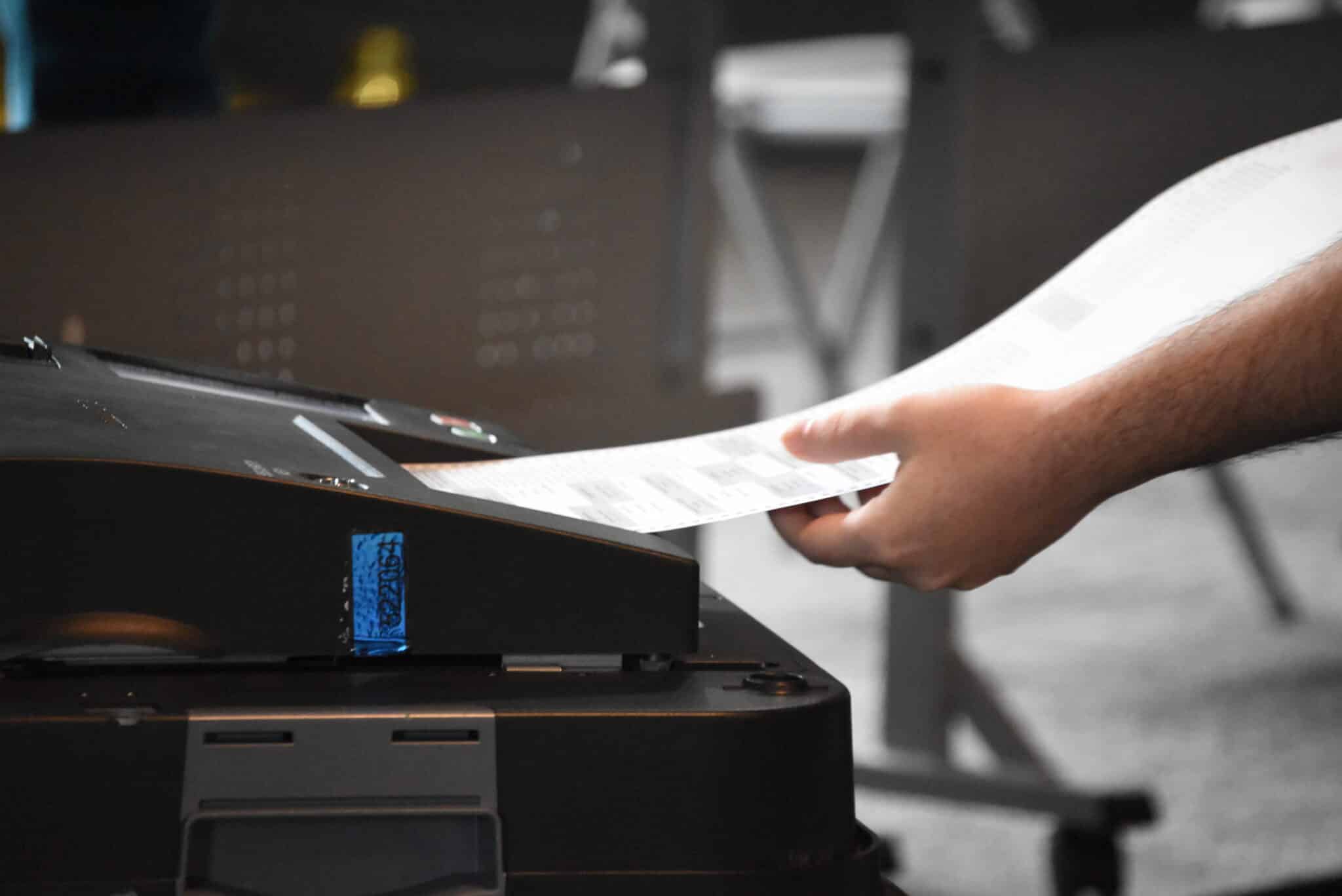 May contain one person inserting a ballot into a machine.
