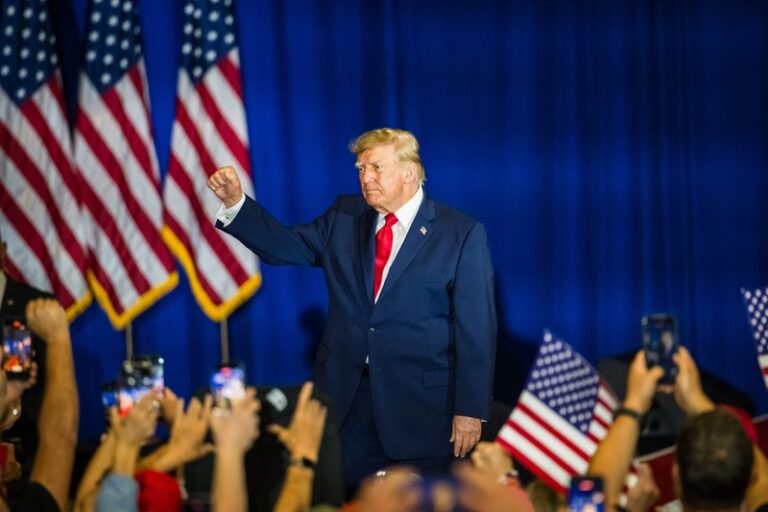 May contain one person raising a fist in front of American flags and a crowd.